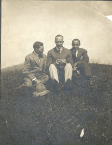 Three men with short hair wearing suits sitting on a hill